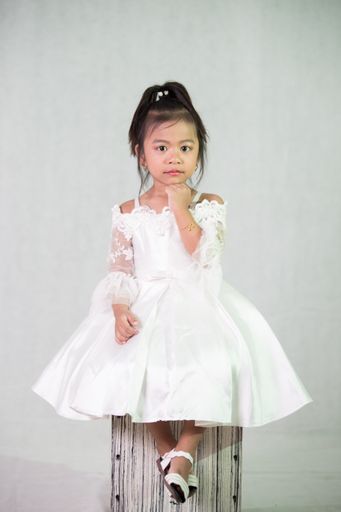 A vertical shot of an adorable Southeast Asian baby girl wearing a white dress