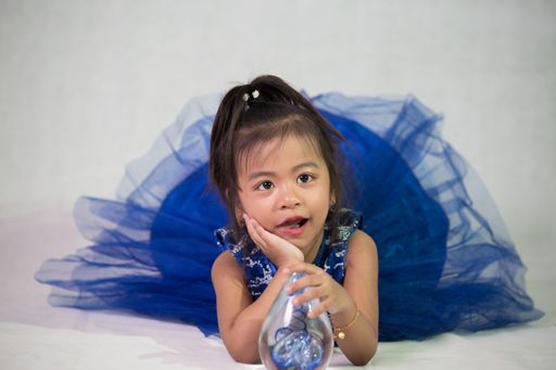 A beautiful shot of an adorable Southeast Asian baby girl wearing a blue dress and laying down