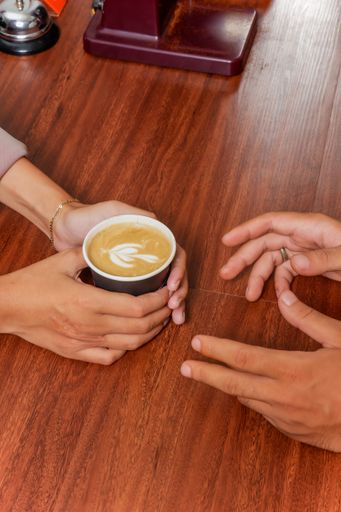A male wearing receiving a cup of steaming hot coffee from another person