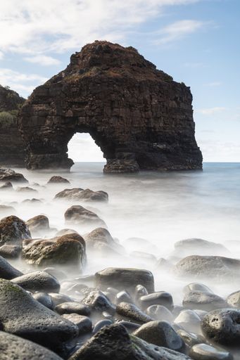 A vertical shot of a rock formation in the middle of the boundless sea