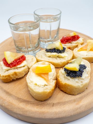 A vertical shot of freshly made sandwiches with fish roes and vodka on a wooden board