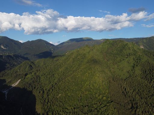 An aerial view of majestic mountain range covered by foliage under the cloudy blue sky