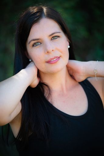 A brunette female wearing a black top and posing in the green park
