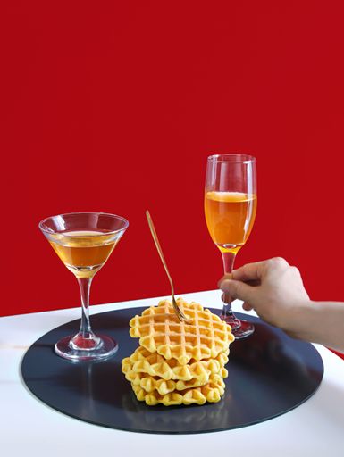 High-resolution vertical shot of a delicious plate of waffles, accompanied by drinks, isolated against a vibrant red background