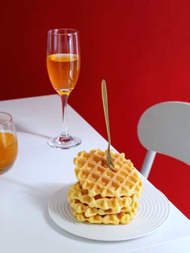 High-resolution vertical shot of a delicious plate of waffles, accompanied by drinks, isolated against a vibrant red background