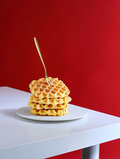 A stack of freshly made Belgian waffles, topped with a small spoon, on a white plate