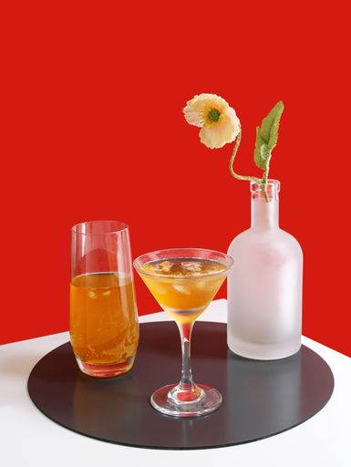 A vertical shot of a pair of glasses with drinks and a vase isolated on red background