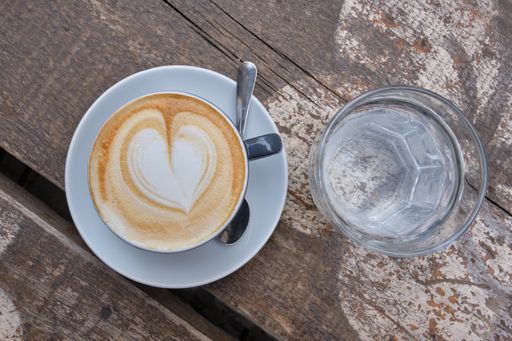 A top view of a cup of delicious cappuccino with heart foam and a glass of water on a wooden surface