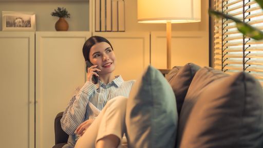 A young female laying on a comfortable sofa while talking on a mobile phone.