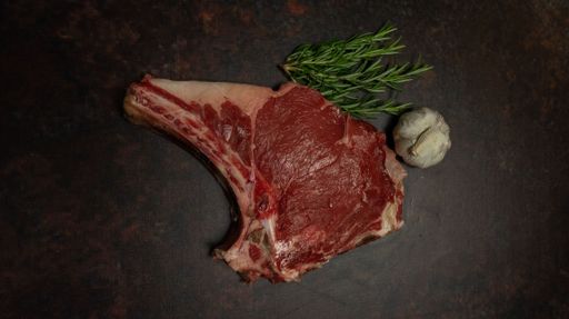 An overhead view of a raw beef steak flavored with garlic and rosemary placed on a black surface