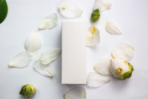 A high-angle view of a white cardboard box with camellia petals and flowers, on a white background,