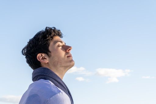 Portrait of young boy with head to the sky and eyes closed on a clear day with blue sky and some white cloud