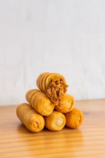 Vertical shot Venezuelan tequenos made of pulled pork piled up on wooden table and light background. Close up.