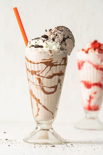 A glass of freshly prepared chocolate milkshake, with chocolate flakes and a straw