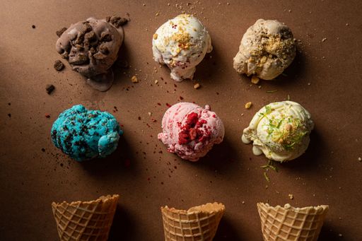 A top view of colorful ice cream scoops with freshly-baked cones arranged on the brown background