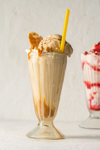 A glass of a creamy orange milkshake topped with ice cream