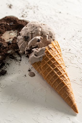 A delicious scoop of chocolate ice cream on a cone near a sprinkling of chocolate shavings