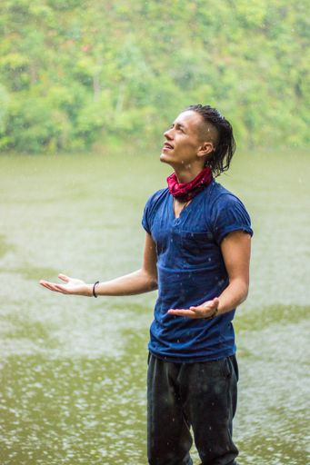 A vertical shot of a Hispanic handsome man with cool haircut enjoying the rain standing by the lake