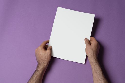 Male hands holding a closed tri-fold catalog with blank cover on purple background