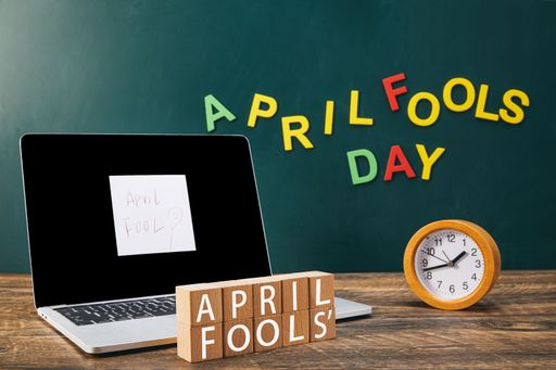 An April Fools wooden text with laptop and clock on a table