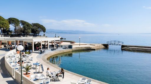 People in cafe near sea. Calm sea on beautiful sunny day in spring. Tourism on adriatic sea coast in Opatija, Croatia.