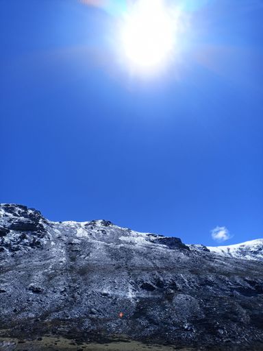 A picturesque landscape of a mountain peak with a single white dot illuminated by the bright rays of the sun