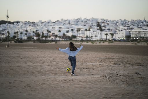 A back view of a young girl playing with a ball on a sandy beach