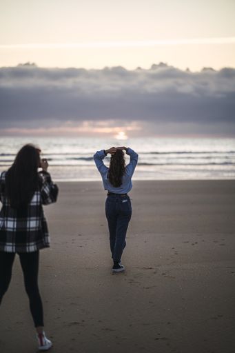 A vertical shot of a young female photographing her friend on the beach at sunset
