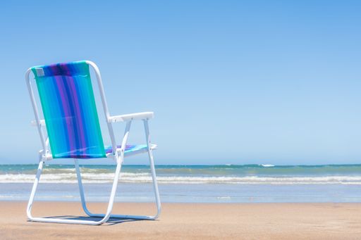 A colorful deckchair with thermos and matte on the sand overlooking the sky and the sea.