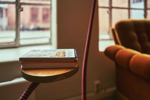 A stack of books sits atop a lamp table in a cozy living room setting
