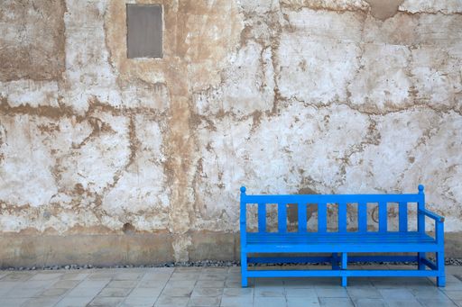 An attractive, light blue bench situated in front of a grand stucco wall in a sunny outdoor setting