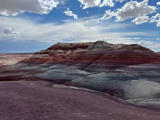 A scenic desert landscape with hills and a bright blue sky with white clouds scattered throughout