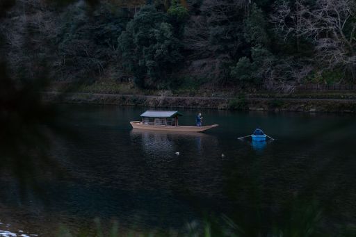 A group of people in a small boat leisurely paddling on a tranquil body of water in Kyoto, Japan.