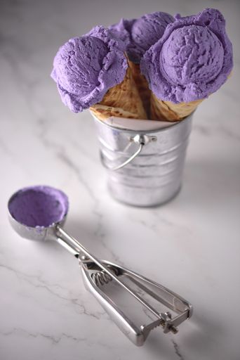 A vertical shot of three violet ice cream cones on a metal container with a spoon isolated on a table