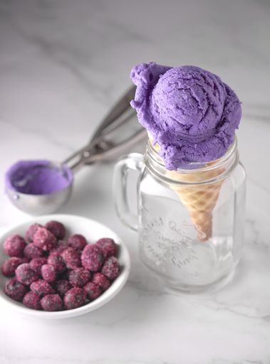 A vertical shot of a violet ice cream cone in a glass cup with berries on a plate