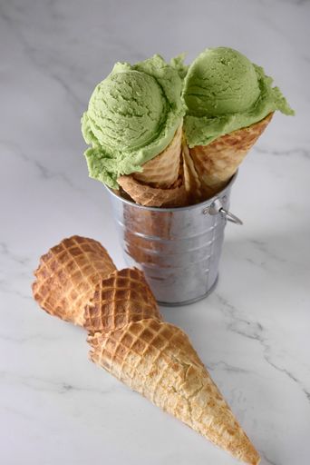 A vertical shot of two green ice cream cones on a metal container with empty cones on the table