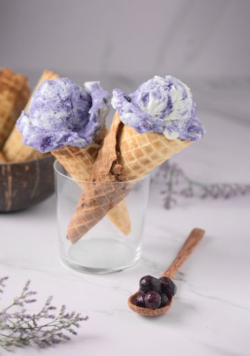 A vertical shot of two violet ice cream cones on a glass and a wooden spoon with berries
