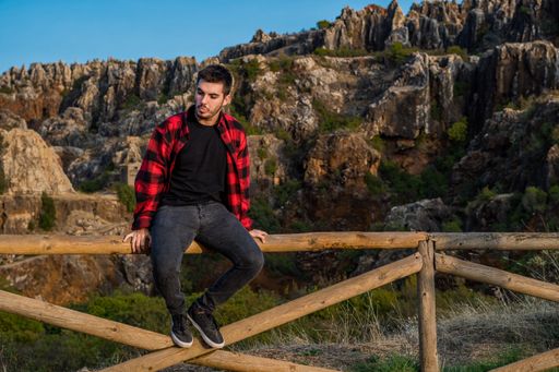 A young Caucasian man from Spain sitting on a wooden fence in mountains and thinking