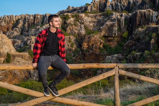 A young Caucasian Spanish man on a wooden fence admiring the mountain view