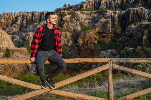 A young Caucasian Spanish man on a wooden fence admiring the mountain view