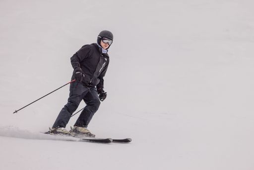 A skier wearing goggles is captured skiing down a snow-covered slope against a backdrop of an overcast sky