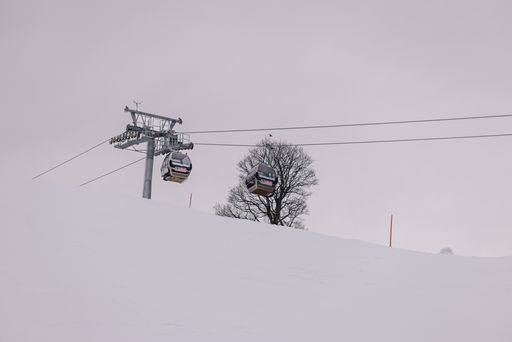 A picturesque winter scene featuring a ski lift ascending a snow-covered mountain range, with evergreen trees in the foreground