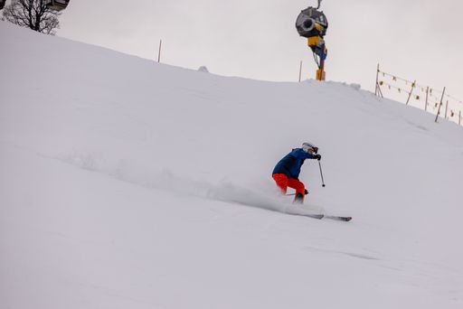 A young man wearing ski goggles and winter apparel takes a scenic ride down a snowy mountain slope on a pair of skis