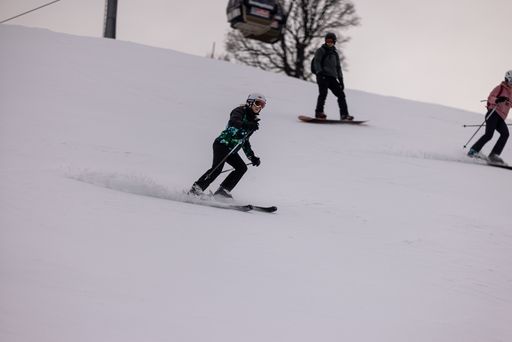 A young man wearing ski goggles and winter apparel takes a scenic ride down a snowy mountain slope on a pair of skis