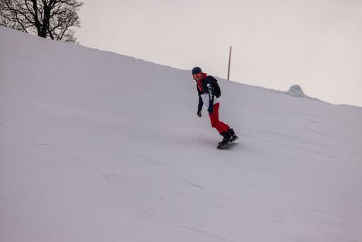 A snowboarder is descending a snowy mountain slope with a bright blue sky in the background