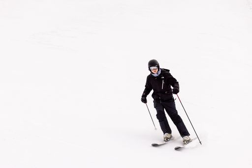 A young man wearing ski goggles and winter apparel takes a scenic ride down a snowy mountain slope on a pair of skis