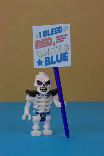 A LEGO skeleton figure holds a sign with "I bleed red, white & blue" phrase