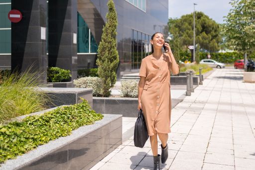 A closeup of a beautiful woman walking down a sidewalk while talking on a cellphone on a sunny day