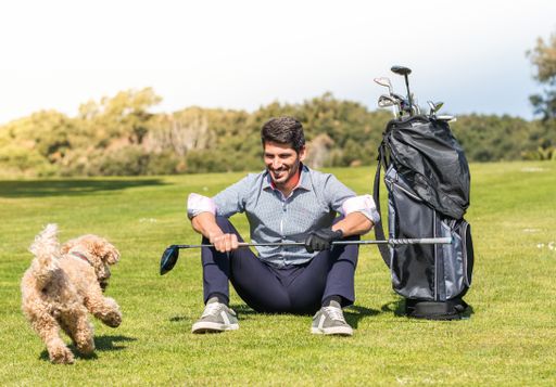 A young Caucasian male playing with his Goldendoodle dog on a professional golf course