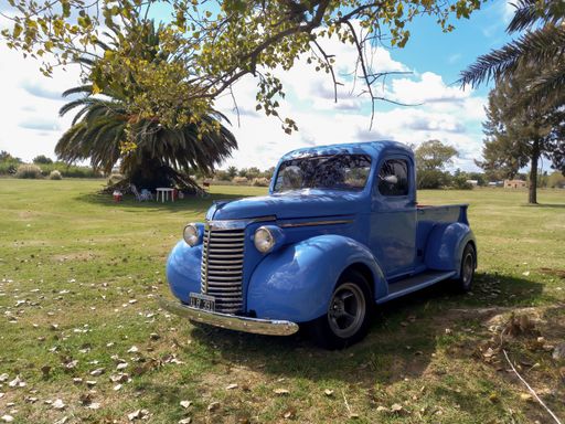 Old blue 1940 Chevrolet Chevy pickup truck hot rod in the countryside under a tree. CAACMACH 2023 classic car show. Sunny day